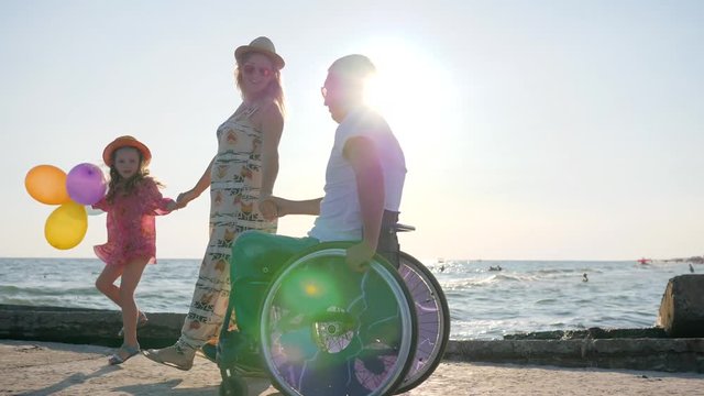 kid at holiday on Sea together with disabled parents, invalid in wheelchair walks with wife and daughter