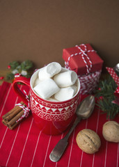 Hot Christmas Beverage Cocoa and Marshmallow in Red Cup with Tea Spoon Presents Boxes Cord Sparkles Nuts Cinnamon Sticks Fir Tree Branch on Dark Background. Winter Time