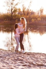 A happy family having fun in the park in autumn walking and hugging. Family, love, happiness concept. Mother and a cute daughter hugging at the sunset near the river in the park