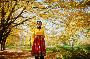 African american girl at yellow and red dress at golden autumn fall park.