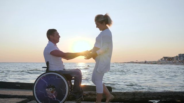 handicapped person in wheelchair listens belly of his wife on background sea, invalid love,