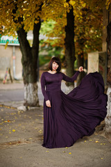 Adult brunette woman at violet gown on autumn fall background.