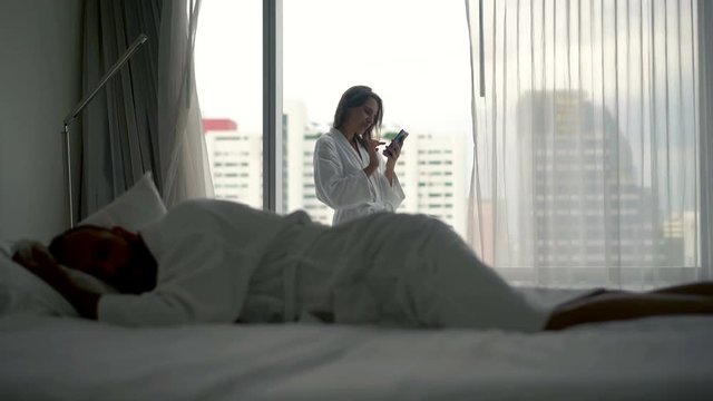 Young woman using smartphone while her boyfriend sleeping 
