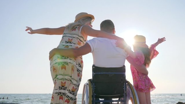disabled hugs wife and daughter invalid with pregnant woman on background sea happy family raising hands