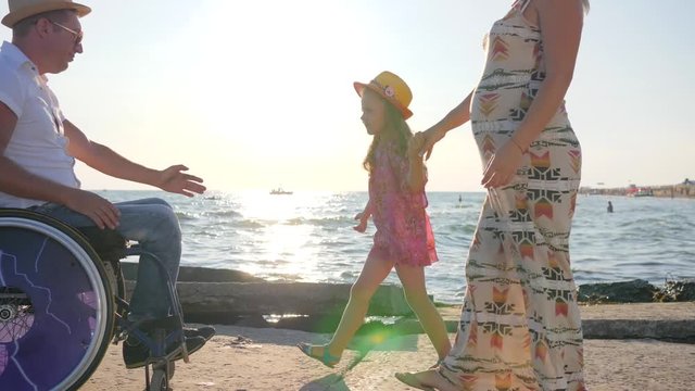 dad with Child hold to mothers belly, man in wheelchair with little Girl and pregnant woman outdoors