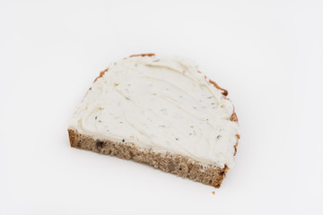 Close up of half a slice of typical German sunflower seed wholegrain bread with herbed cream cheese spread isolated on white background