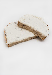 Two halved slices of typical German sunflower seed wholegrain bread with herbed cream cheese spread isolated on white background