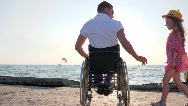 disabled spouse hugs his pregnant wife with big belly and daughter at sunset