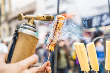 A chef grilling cheese with a kitchen gas torch at a food market