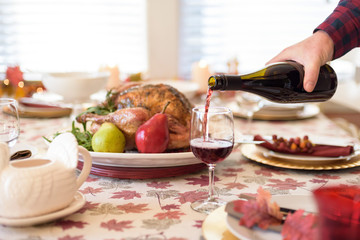 Pouring red wine into a glass at a holiday dinner featuring turkey