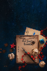 New Year resolution concept with retro notepad, letters to Santa, inkwell and pen. Christmas celebration dark flat lay with presents, stars, decorations and copy space.