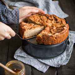 Homemade cake with whole wheat flour with apples on a wooden background. Food photo with hands and flowers. Useful dietary baking.