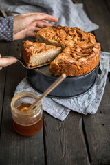 Homemade cake with whole wheat flour with apples on a wooden background. Food photo with hands and flowers. Useful dietary baking.