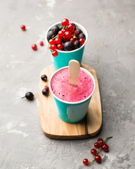 Frozen berry smoothies in bright paper cups on a light gray concrete background with fresh red currant and black gooseberry. place for text, top view