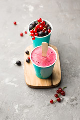 Frozen berry smoothies in bright paper cups on a light gray concrete background with fresh red currant and black gooseberry. place for text, top view
