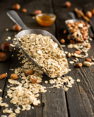Natural products in iron vintage scoops on wooden granary boards. Hercules flakes (oat flakes), sunflower seeds, fresh peanuts, hazelnuts, honey. Ingredients for granola or oatmeal. Useful breakfast.