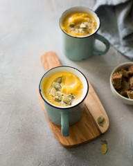 Pumpkin soup with coconut milk, pumpkin seeds and spices in vintage blue mugs on a gray concrete background. Atmospheric dark food photo. 