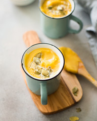 Pumpkin soup with coconut milk, pumpkin seeds and spices in vintage blue mugs on a gray concrete background. Atmospheric dark food photo. 