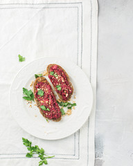 Homemade toast from whole grain bread with beet paste, greens and nuts. Light concrete background, white soft. Place for text. Food photo with hands. Useful dietary baking. Flat lay, top view