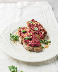 Homemade toast from whole grain bread with beet paste, greens and nuts. Light concrete background, white soft. Place for text. Food photo with hands. Useful dietary baking. Flat lay, top view