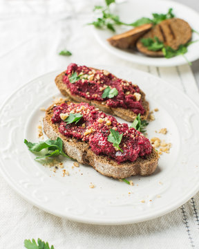 Homemade toast from whole grain bread with beet paste, greens and nuts. Light concrete background, white soft. Place for text. Food photo with hands. Useful dietary baking. Flat lay, top view