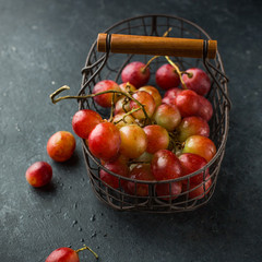 Red large grapes on a branch in a vintage iron basket on a concrete black background. Fresh fruits, beautiful card or background