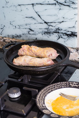 Stuffed and battered chicken breast being cooked in a cast iron skillet