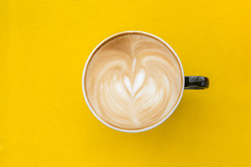 A cup of heart-shaped coffee in a red cup on a yellow wooden floor.