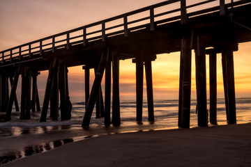 Sunset beach view through pier silhouette
