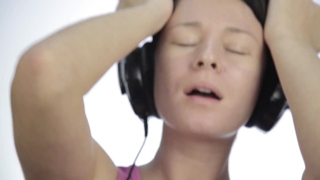 brunette woman listening music with big headphones and dancing on a light background