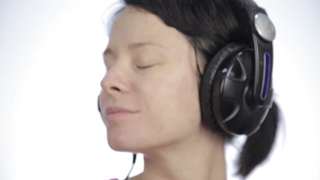brunette woman listening music with big headphones and dancing on a light background