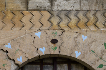 detail of a stone architecture. ashlar stone with decoration. heart and leave grafitti on a stone door.  zig zag and rounded lines on yellow stone.