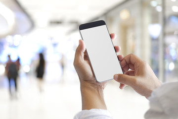 Mockup image of hands holding black mobile phone with blank white screen in shopping mall.
