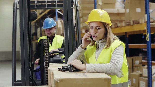 Young workers with smartphone and forklift in warehouse.