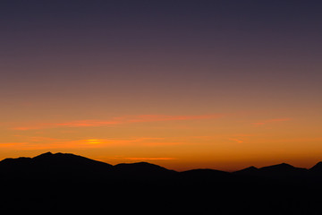 A silhouette of a mountain peak at sunset, under a big sky with beautiful tones and colors
