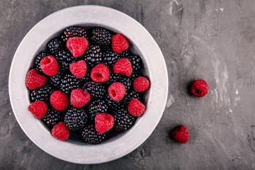 fresh ripe organic raspberries and blackberries in a bowl on a gray background