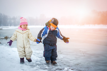 Little girl and boy holding hands while walking near frozen river in the winter park. © Bojan