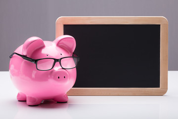 Piggybank With Eyeglasses Near Blank Slate