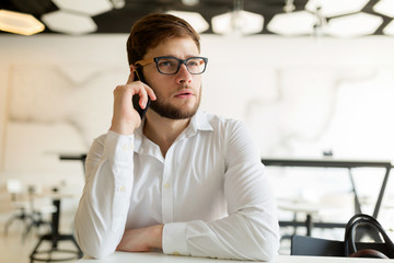 Pensive young businessman in cafe using phone