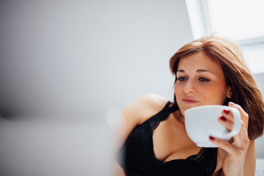 Young female laying on bed while drinking coffee