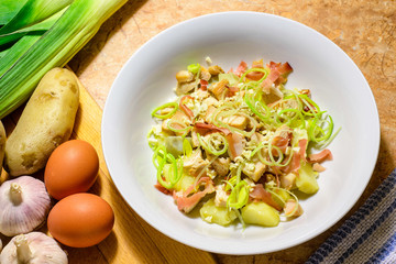 Chicken salad with speck, garlic, potatoes and leeks in a white porcelain dish