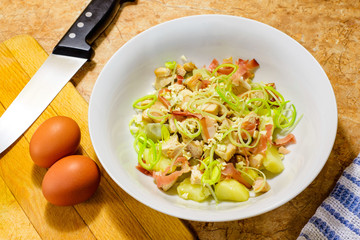 Chicken salad with speck, garlic, potatoes and leeks in a white porcelain dish