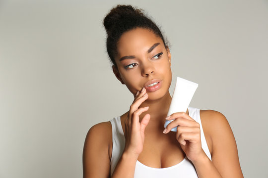 Beautiful Young African American Woman Holding Bottle With Cream On Light Background