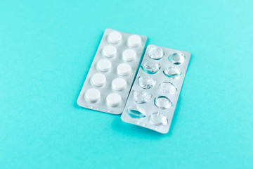 Full and empty packs of white pills packed in blisters with copy space on turquoise background. Focus on foreground, soft bokeh. Pharmacy drugstore concept