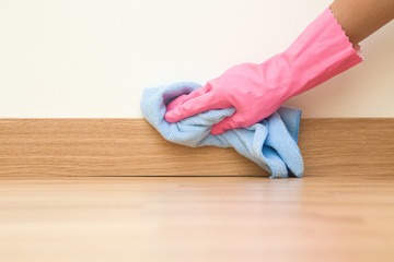 Employee hand in rubber protective glove with micro fiber cloth wiping a baseboard on the floor...