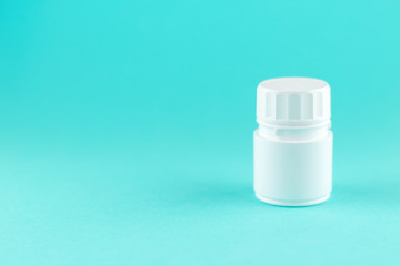 Close up white pill bottle on turquoise background with copy space. Focus on foreground, soft bokeh. Pharmacy drugstore concept