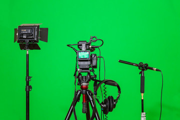 The camera on the tripod, led floodlight, headphones and a directional microphone on a green background. The chroma key. Green screen.