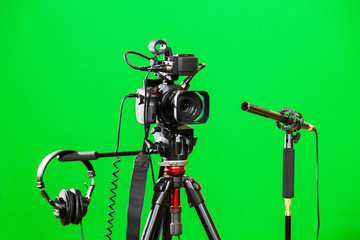 Video camera on a tripod, headphones and a directional microphone on a green background. The chroma...