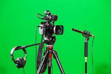 Video camera on a tripod, headphones and a directional microphone on a green background. The chroma...