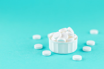 Fototapeta na wymiar Close up white pills and capsules in cap on turquoise background with copy space. Focus on foreground, soft bokeh. Pharmacy drugstore concept